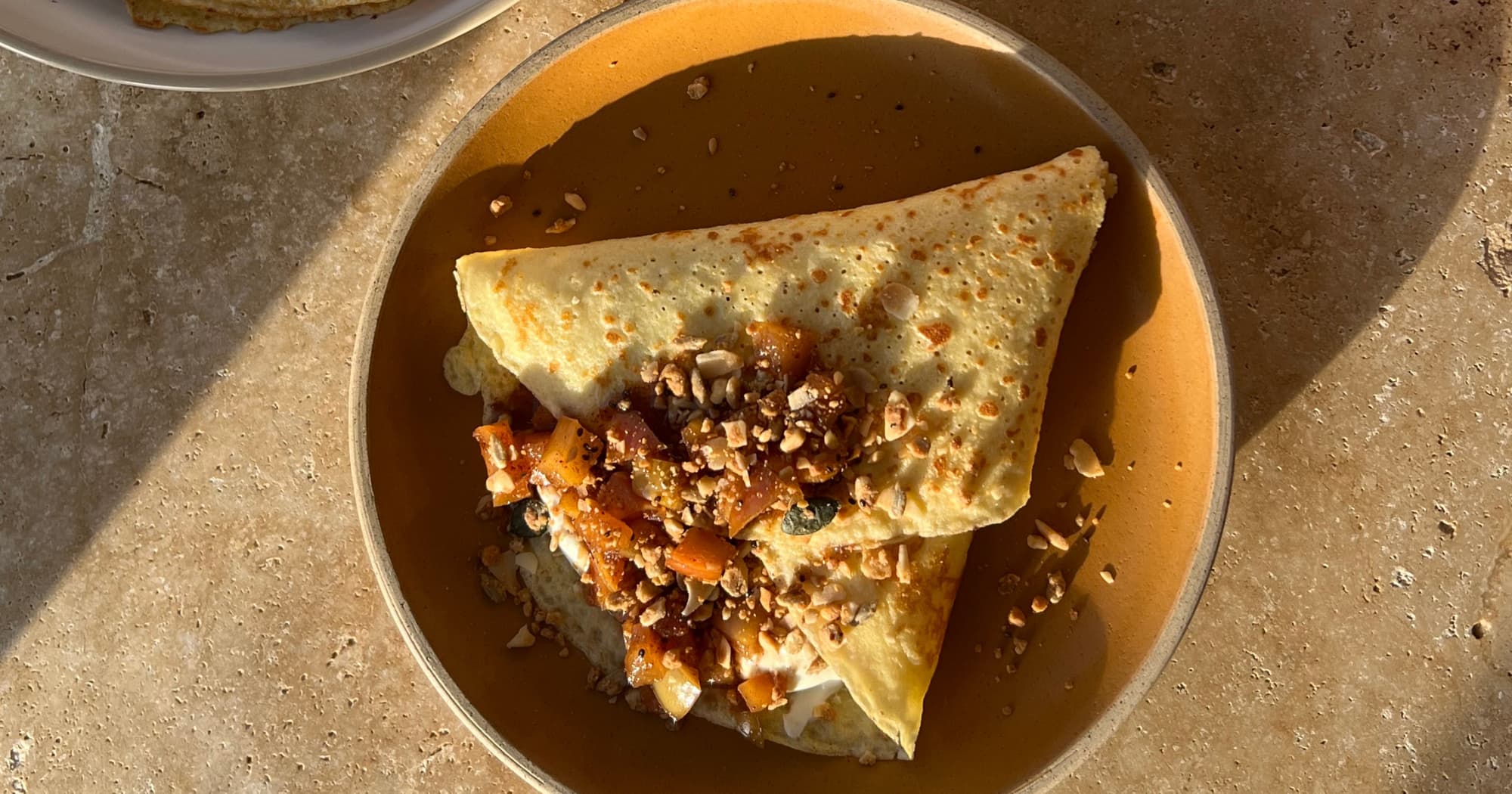Folded almond flour crepe on a plate, filled with yoghurt and topped with diced stewed apple and granola 
