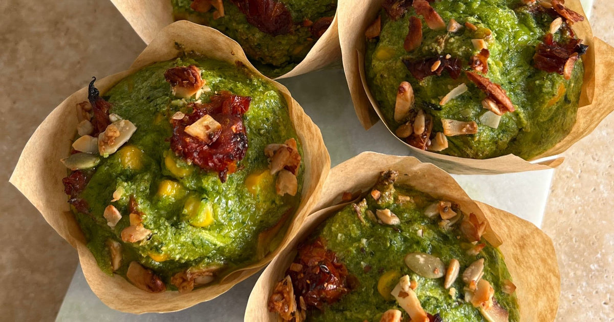 Four grain-free sundried tomato and spinach muffins in brown paper cases, topped with sundried tomato pieces and Paleo Foods Co granola