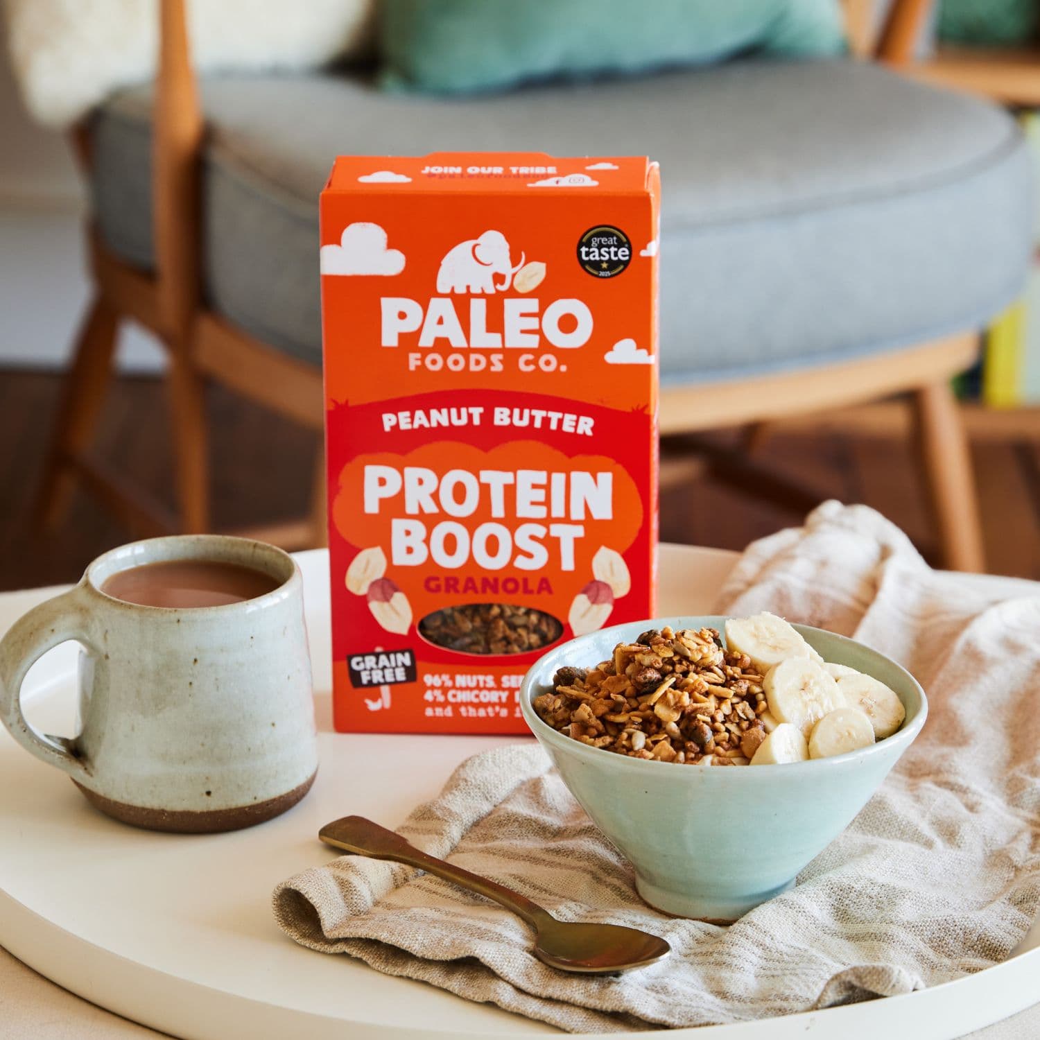 Paleo Foods Co. Peanut Butter Protein Boost Granola with a bowl of cereal and coffee on a table.